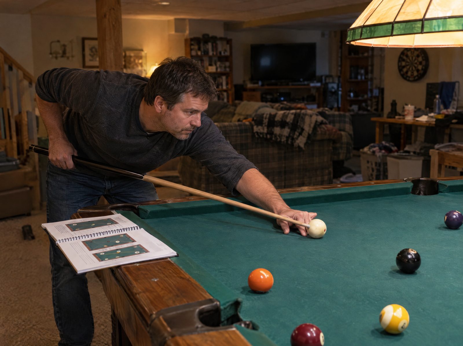 A player at a home pool table with the practice book open on the rail