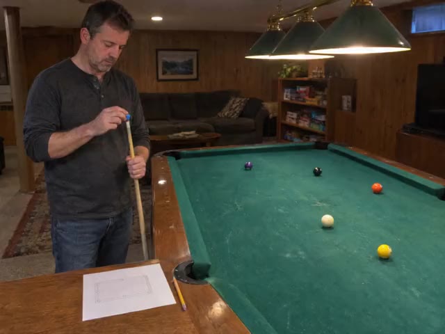 A player chalking his cue at a home pool table, a drill page on the rail